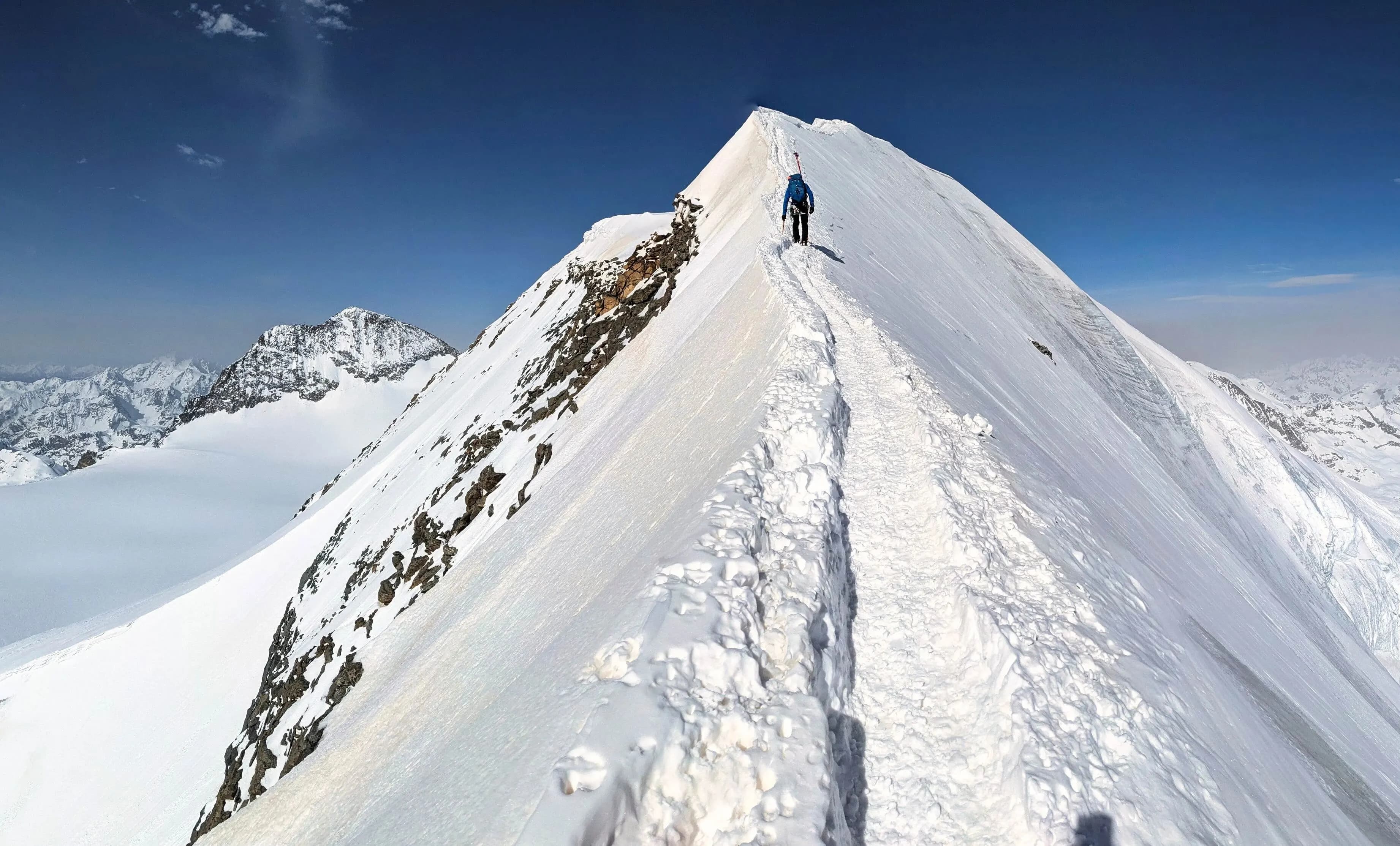 Image of a climber hiking to the top of a snowy mountain pictured from the back